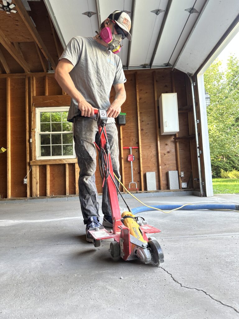 Aidan using a crack-chasing grinder to prepare a concrete garage floor crack for repair in Rochester, New York